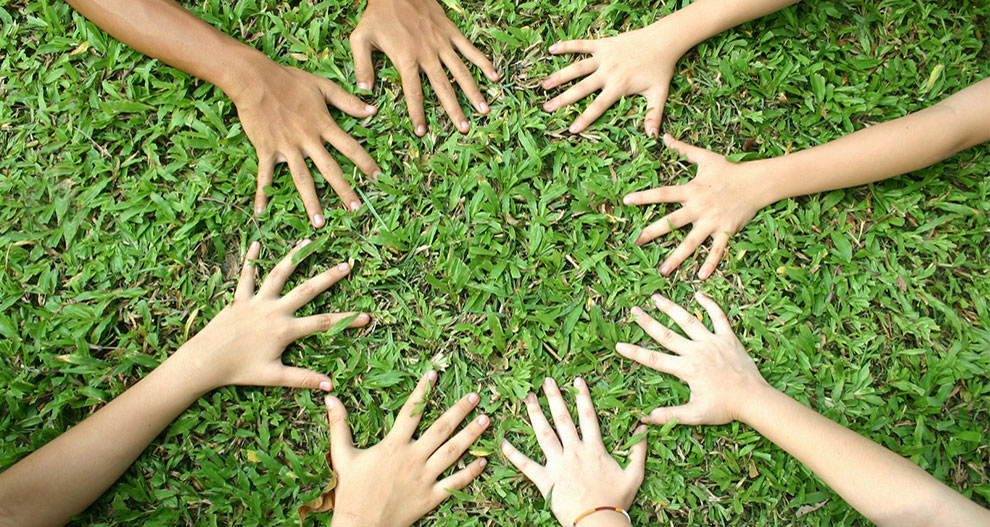 Several hands are placed on a grassy surface, forming a pattern.
